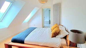Et soveværelse med skråvæg, ovenlys, en seng med træramme, en sengebordlampe og en radiator.