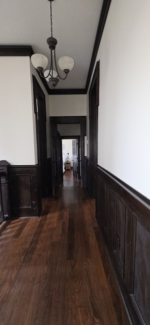 A wooden hallway with a chandelier, dark wood paneling, and a door at the end.