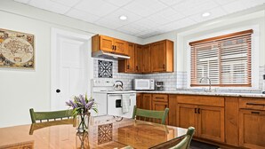 Una cocina moderna con armarios de madera, un microondas y una estufa. Hay una mesa de comedor con sillas y un jarrón con flores.