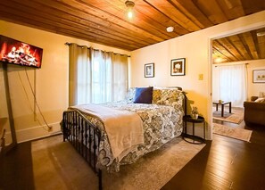 A bedroom with a bed, a TV, a window with curtains, and a door leading to another room.