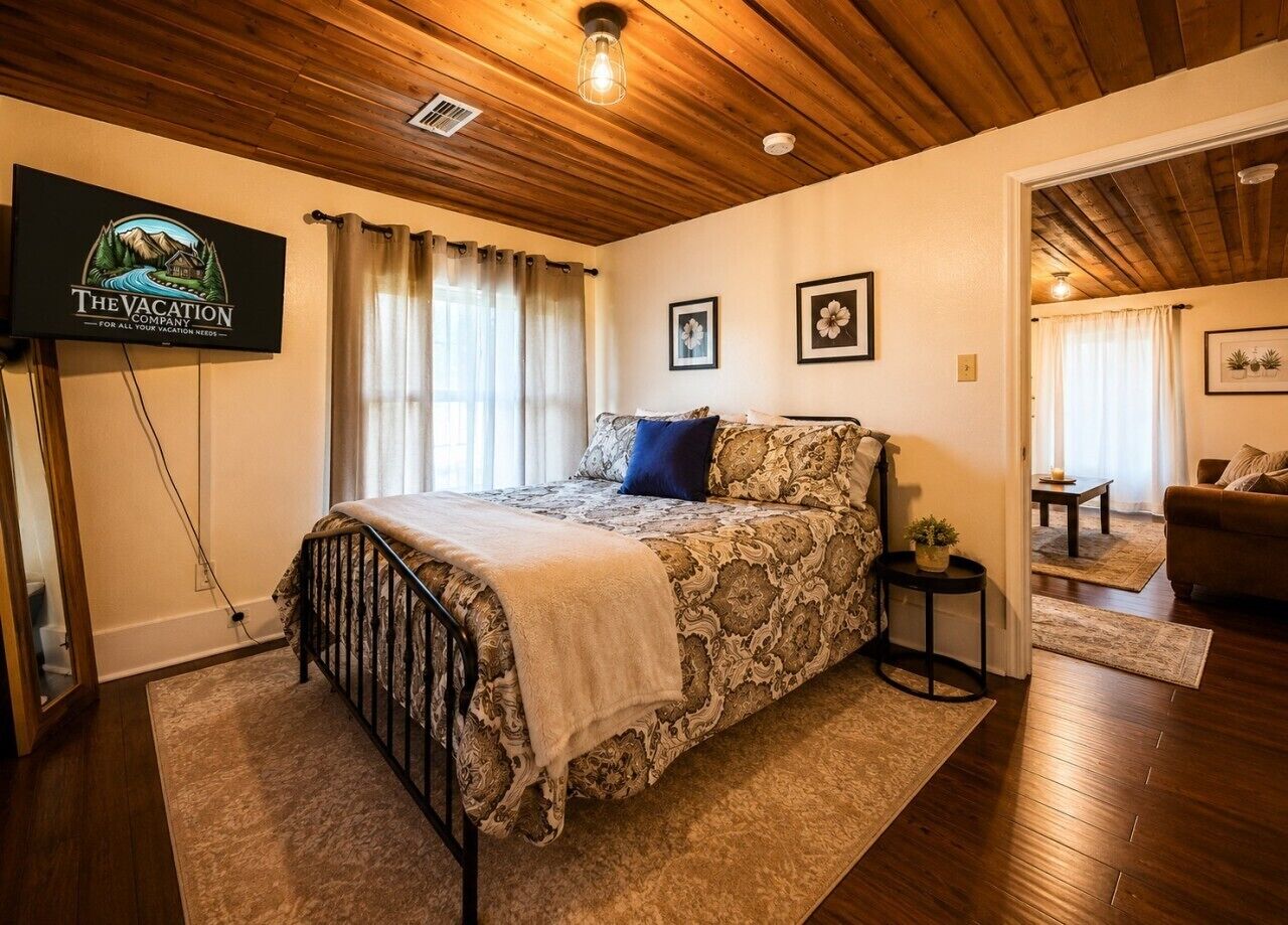 Une chambre à coucher avec un lit, un téléviseur fixé au mur et un plafond en bois.