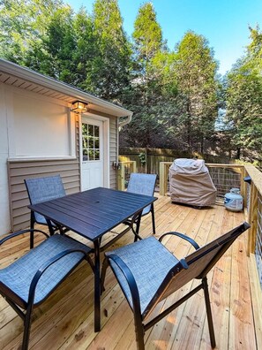 A wooden deck with a table and chairs, a covered grill, and a house in the background.