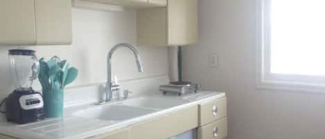 A kitchen with a sink, a blender, and a window.
