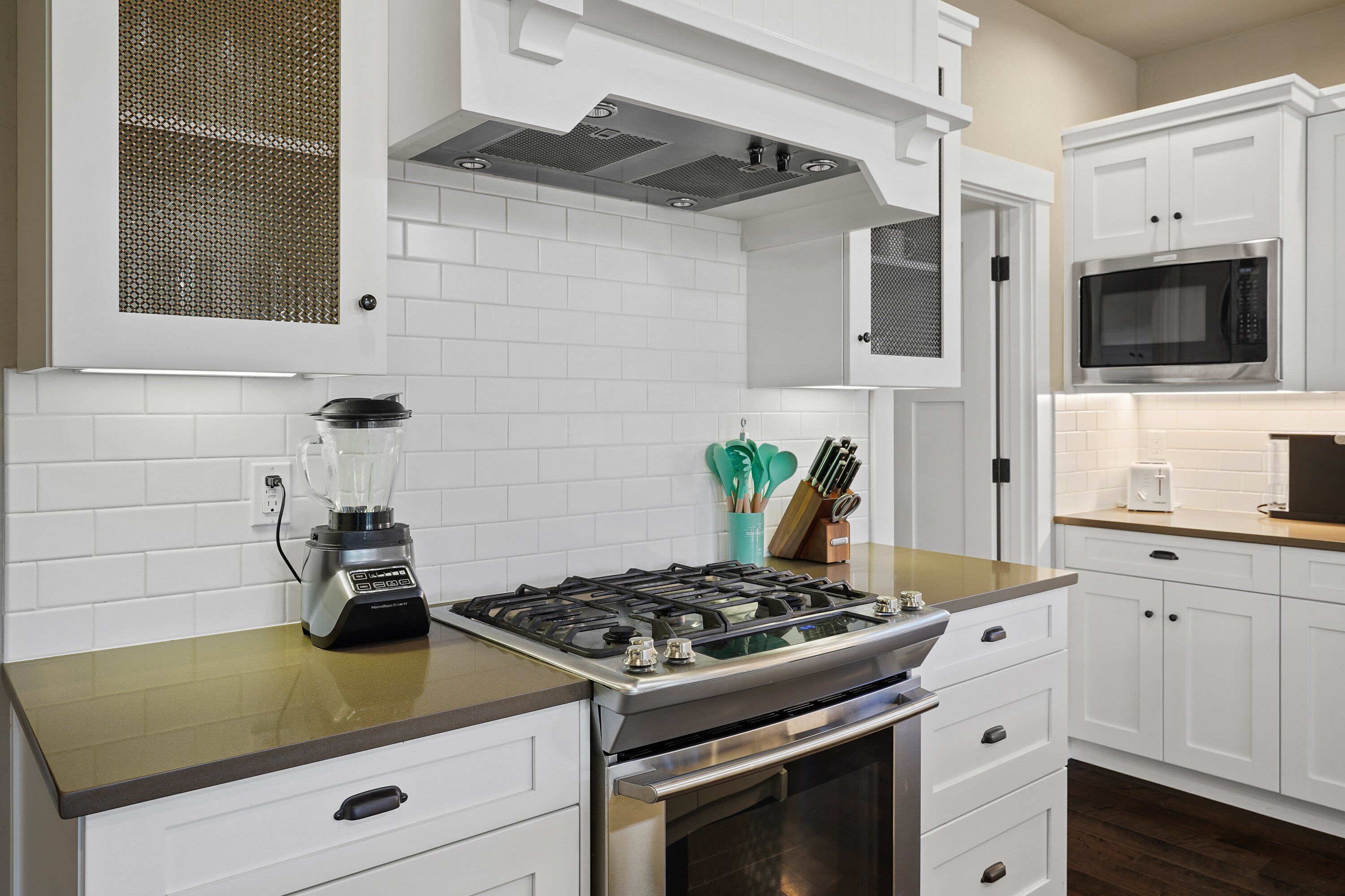 A modern kitchen with white cabinets, a gas stove, a microwave, and a blender on the counter.