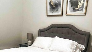 A neatly made bed with white bedding, a wooden bench, a nightstand with a lamp, and two abstract paintings on the wall. - Entire One Bedroom Condo with Private Roofdeck (Boston)
