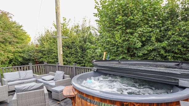 Un bain à remous sur une terrasse en bois, agrémentée de meubles en osier et d’une clôture en bois.