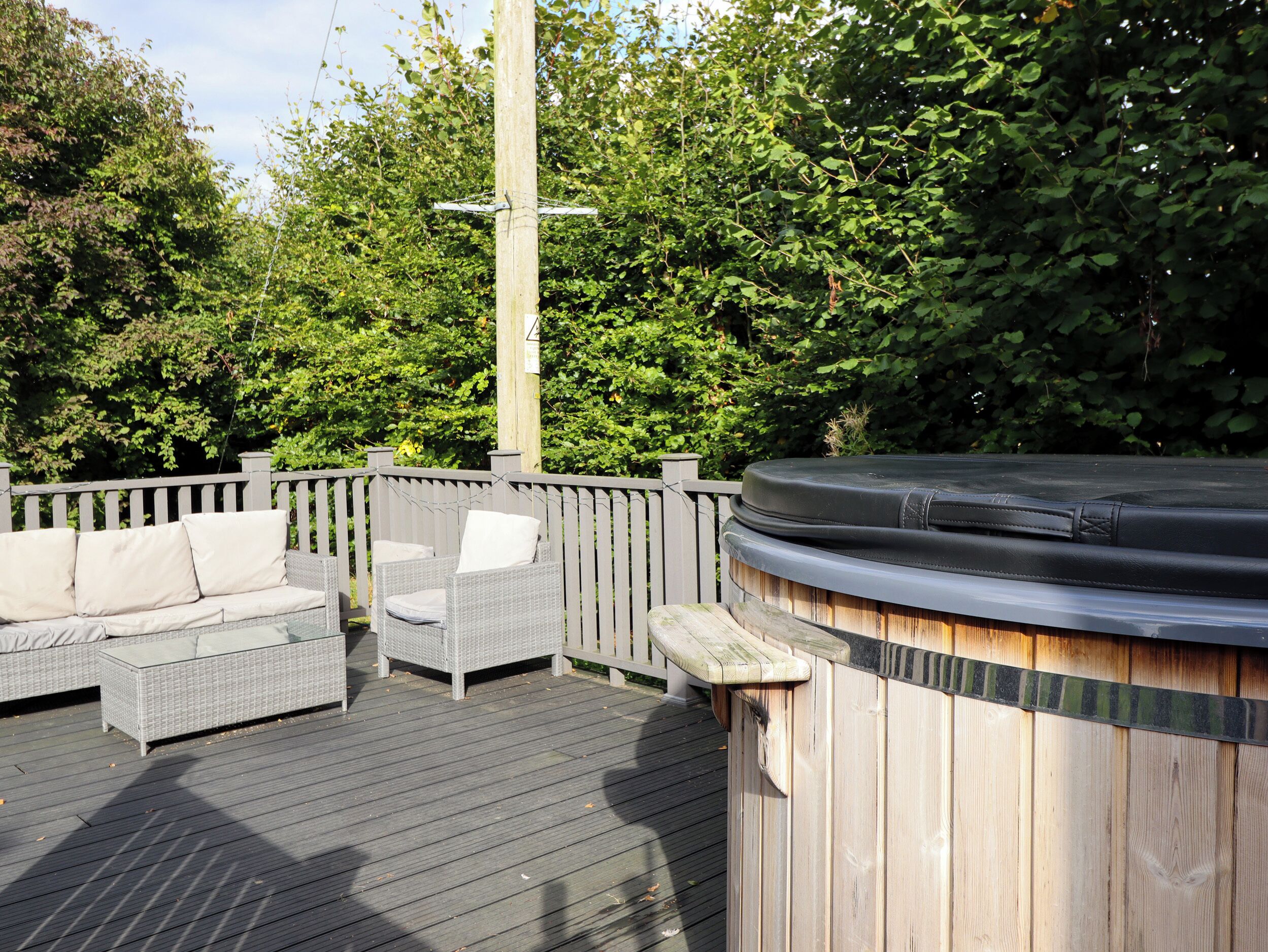 Une terrasse extérieure avec un bain à remous en bois, des meubles en osier et une clôture en bois.