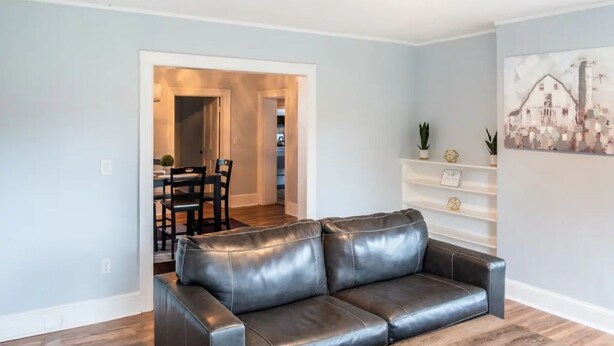 A living room with a dark leather sofa, a wooden coffee table, and a dining area with a table and chairs. - Simple Modern Elegance with Hudson Valley Mountains backdrop, 3rd Fl (Newburgh)