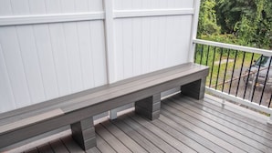 A wooden bench on a covered porch with white paneling and a metal railing. - Modern Modest Design  Newburgh, Beacon, Westpoint  2nd. FL Apt. (Newburgh)