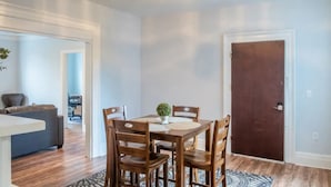 A dining area with a wooden table and chairs, a small plant on the table, and a patterned rug on the floor. - Modern Modest Design  Newburgh, Beacon, Westpoint  2nd. FL Apt. (Newburgh)