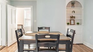 Une salle à manger avec une table en bois et quatre chaises, une porte blanche et une étagère blanche ornée d’objets décoratifs.
