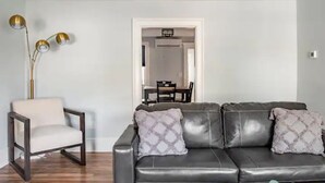 Un salon avec un canapé en cuir foncé, un fauteuil blanc et une lampe sur pied.