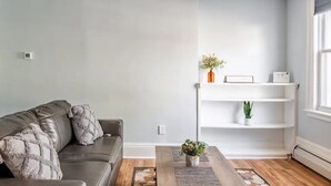 Un salon moderne avec un canapé gris, une table basse en bois et une étagère blanche, le tout placé devant un mur gris clair.