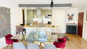 Una cocina moderna con una isla central, un comedor con mesa y sillas de vidrio, y una obra de arte vibrante en la pared.
