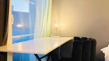 A room with a window, a table, a chair, and a bedside lamp.