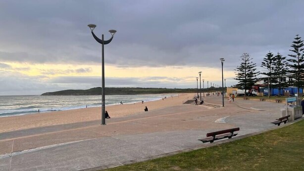 A coastal promenade with a sandy beach, benches, and street lamps.