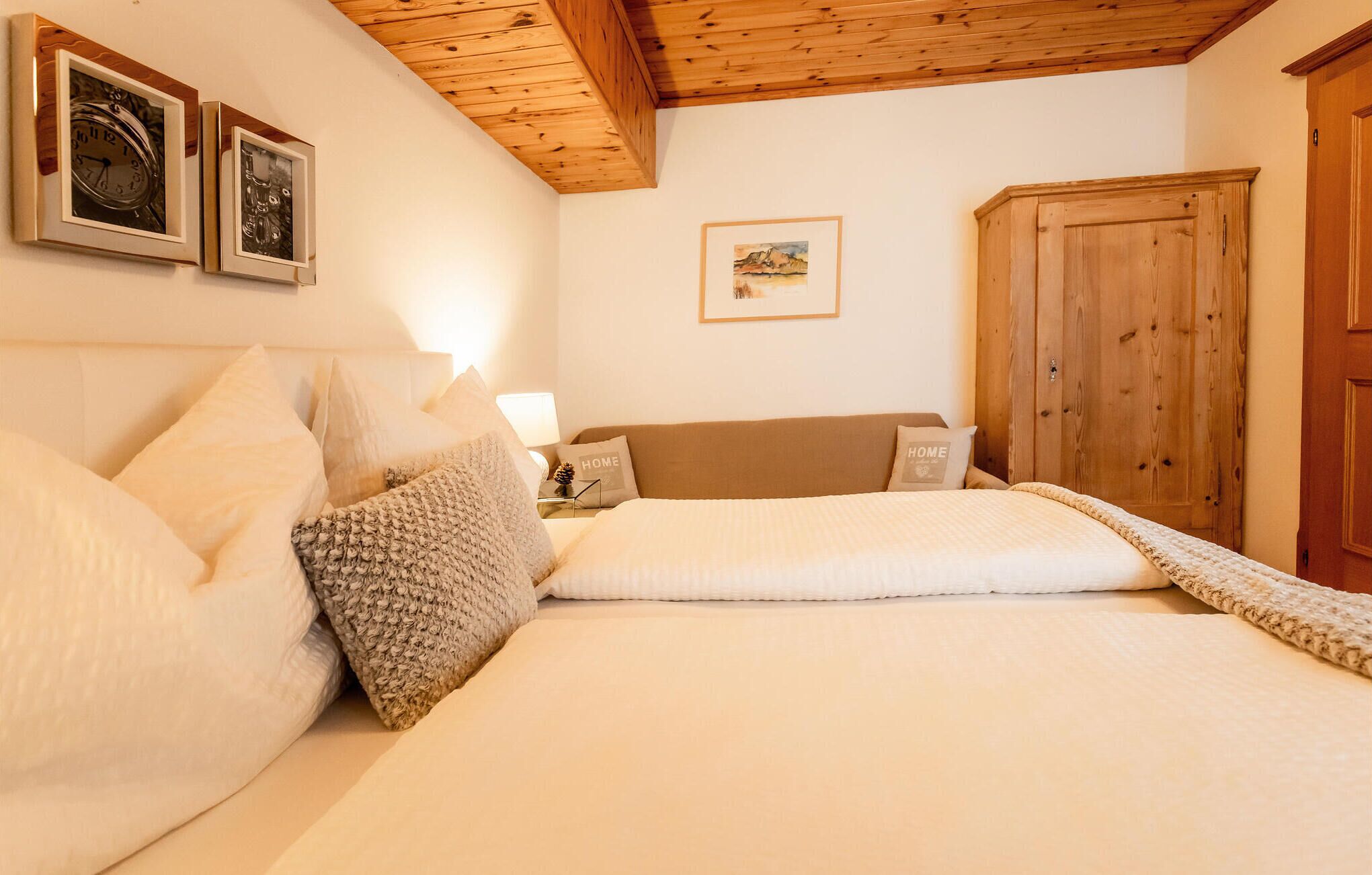 Une chambre avec un plafond en bois, un lit avec une literie blanche, deux horloges au mur et une armoire en bois.