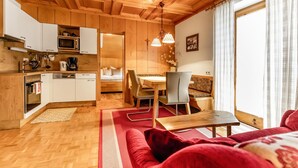 A cozy room with a wooden ceiling, a dining area with a table and chairs, a sofa, and a kitchen with a microwave and cabinets.