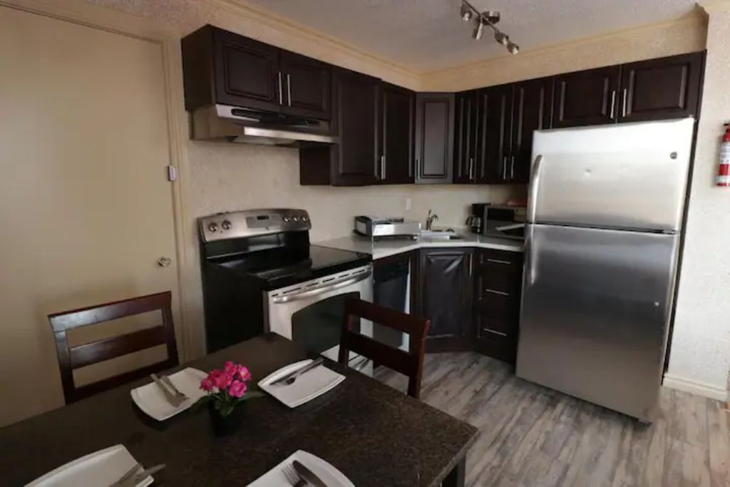 Una cocina compacta con armarios oscuros, un refrigerador de acero inoxidable, una estufa y un tostador.