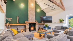 A modern living room with a stone fireplace, grey sofas, a flat-screen TV, and a chandelier. - The Waterfall Retreat (Penrith)