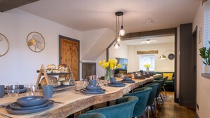 A long dining table with blue chairs, a wooden ceiling, and a view into another room. - The Waterfall Retreat (Penrith)