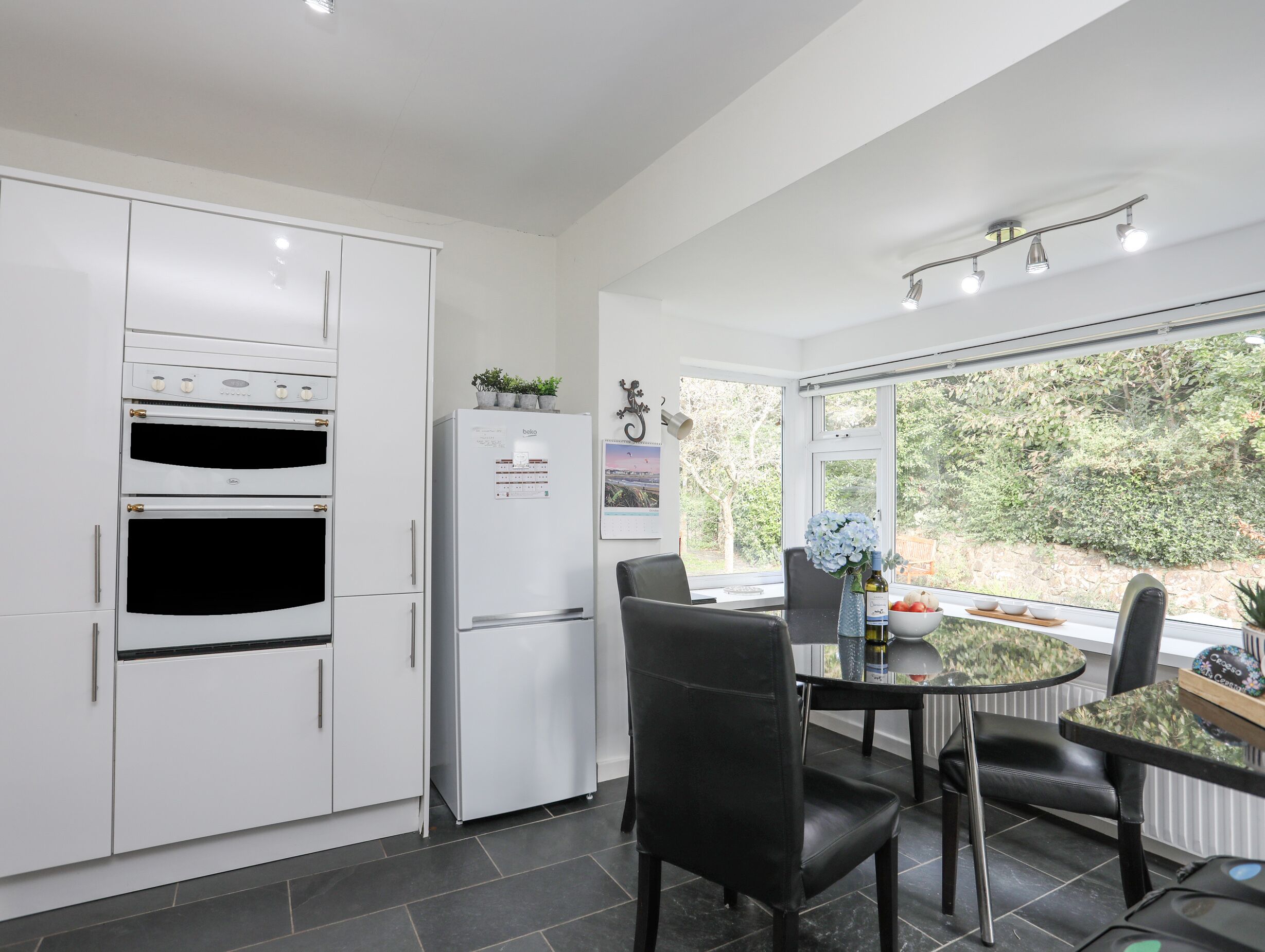 Una cocina moderna con armarios blancos, horno empotrado, refrigerador y un comedor con mesa y sillas.
