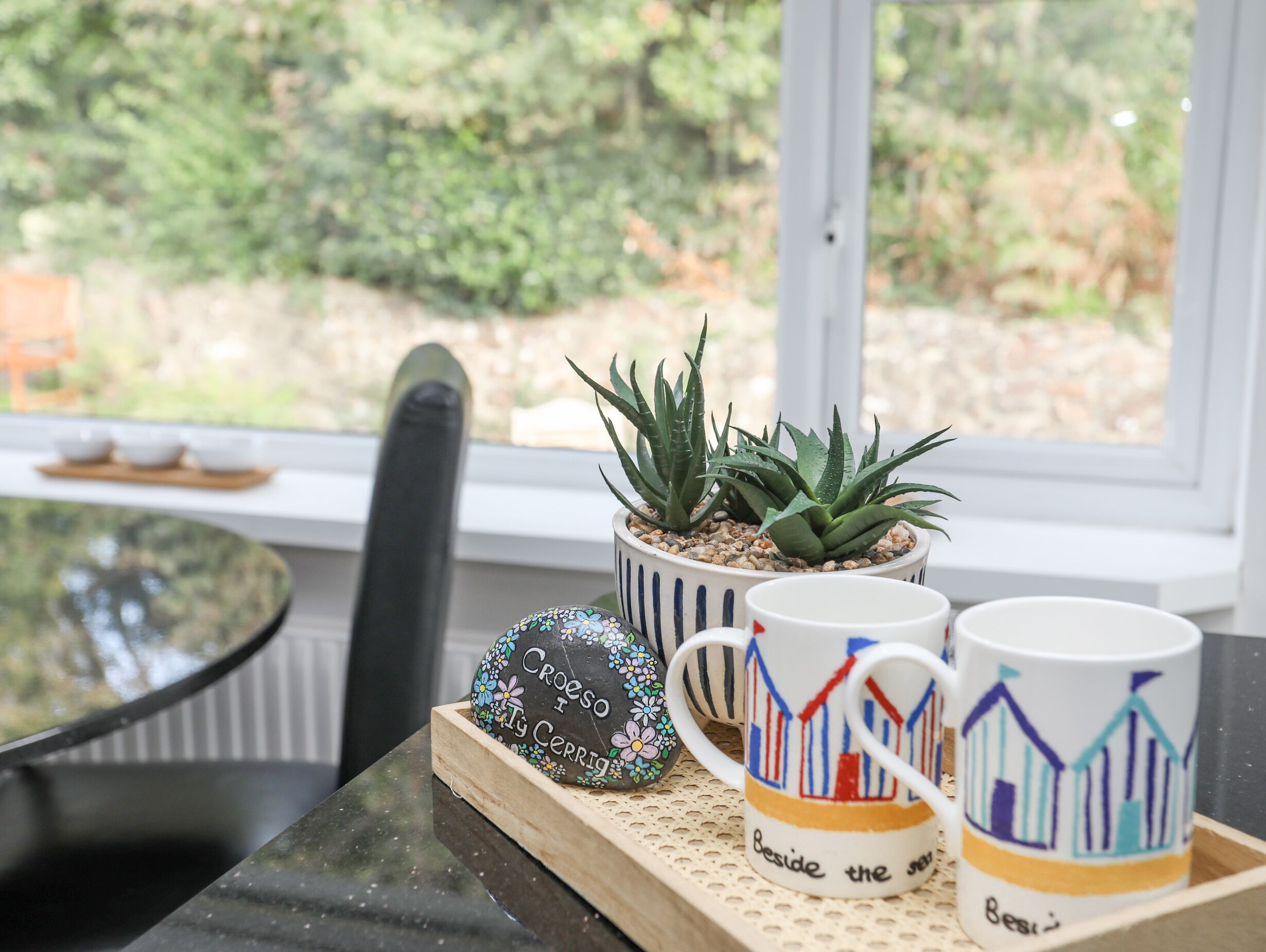 A table with a potted plant, two mugs, and a decorative stone.