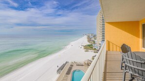 A balcony with a view of a beach and ocean, a pool, and outdoor seating.