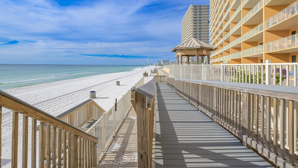 A wooden boardwalk leading to a beach with a hotel in the background.