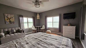 A bedroom with a bed, a sofa, a desk, two chairs, a dresser, and a TV. - Super spacious cabin. Simple layout and great views overlooking the lake! (Faribault)
