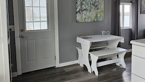 A room with a white door, a white bench, a table, and a grey wall with two paintings. - Super spacious cabin. Simple layout and great views overlooking the lake! (Faribault)