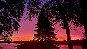 A cabin by a lake at sunset with a view of the water and trees. - Super spacious cabin. Simple layout and great views overlooking the lake! (Faribault)