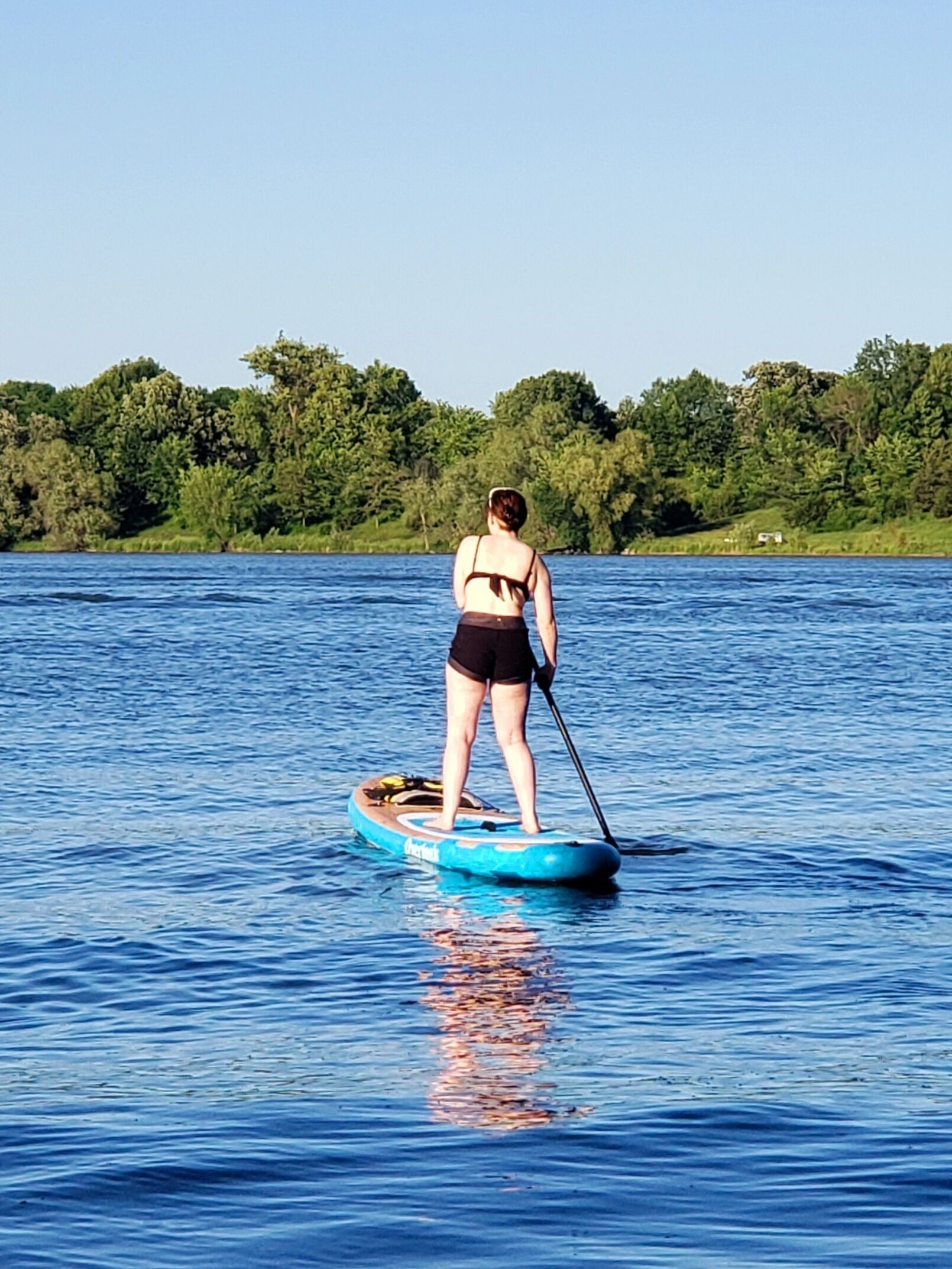 A person paddleboarding on a calm lake with a forested shoreline in the background.