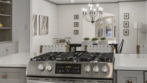Een moderne keuken met een roestvrijstalen fornuis, witte aanrechtbladen en een kroonluchter.