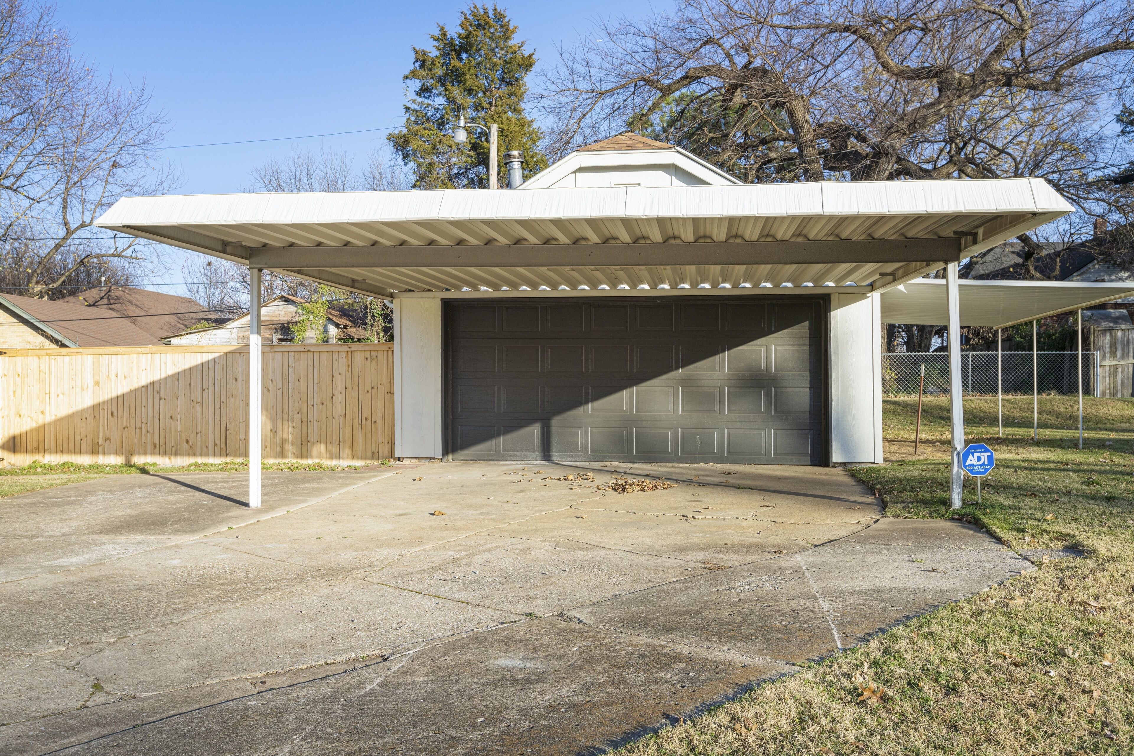 A garage with a covered parking area, a wooden fence, and a clear sky.