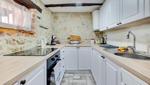 Une cuisine de taille réduite avec des meubles blancs, un mur en pierre et un plafond en bois.
