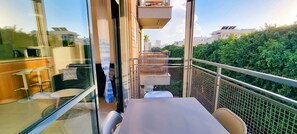 A balcony with a table and chairs, a view of the city, and a mesh railing. - Dizengoff Muguet (Tel Aviv)