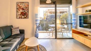 Un salón moderno con sofá, una mesa de centro, un televisor de pantalla plana y un balcón con vistas a la ciudad.