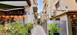 A narrow alleyway with buildings on either side, some with signage and plants in the foreground. - Dizengoff Muguet (Tel Aviv)