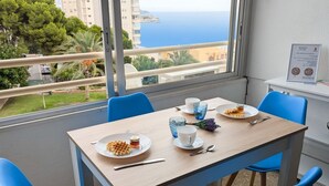 Spisestue med et bord dækket til to, havudsigt og en balkon med blå stole.