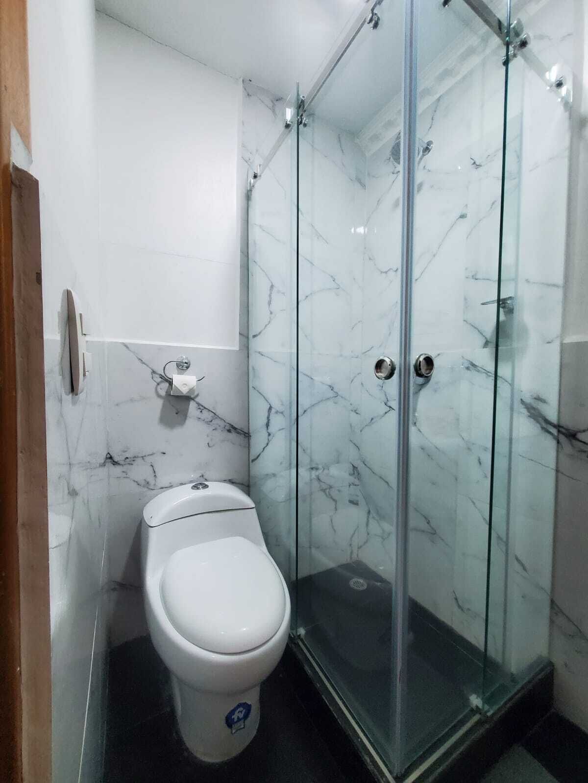 Un baño con inodoro, cabina de ducha de vidrio y paredes de mármol.