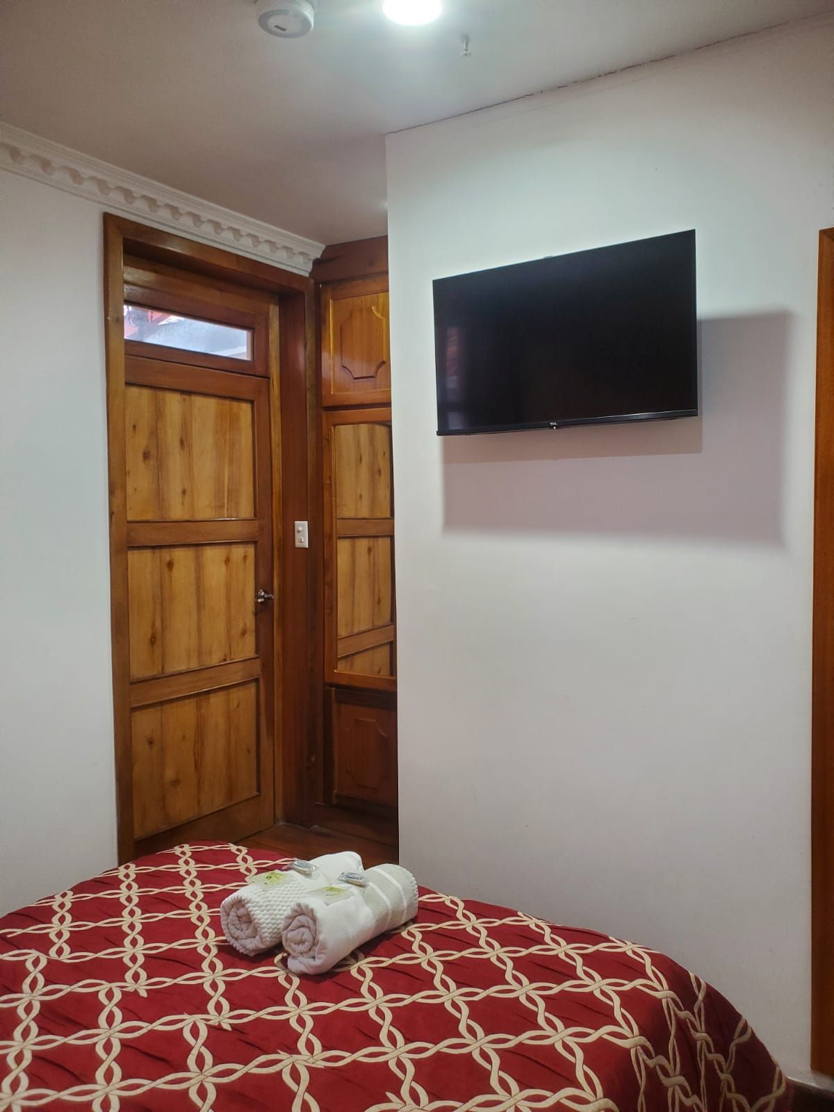 Ein Zimmer mit einem Bett, einem an der Wand montierten Fernseher und einem Holzschrank.