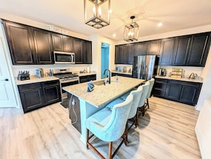 A modern kitchen with dark cabinets, stainless steel appliances, and a central island with bar stools.