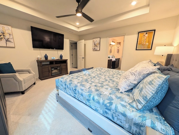 A bedroom with a large bed, a TV, a ceiling fan, and artwork on the walls.