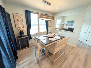 Un coin repas avec une table en bois dressée pour quatre personnes, un meuble noir et une fenêtre avec des rideaux.