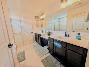 Une salle de bain moderne avec deux vasques, des meubles sombres, un grand miroir et une plante en pot.