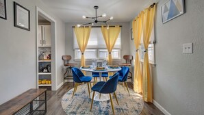 A dining area with a round table, blue chairs, yellow curtains, and a chandelier.