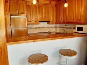 Uma cozinha com armários de madeira, geladeira de aço inoxidável, micro-ondas e dois banquetas.