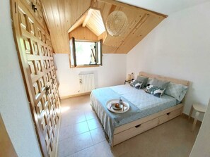 Quarto com teto inclinado, cama com bandeja de café da manhã, radiador e janela.