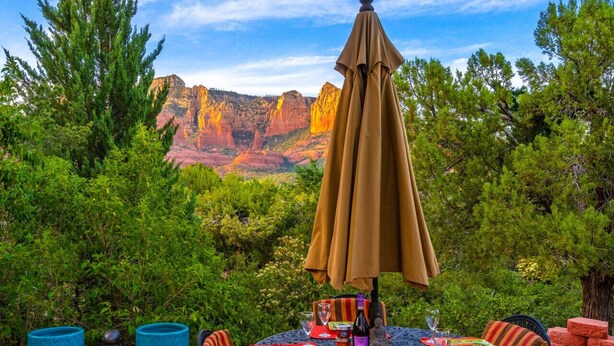 An outdoor dining area with a table set for four, surrounded by chairs, and an umbrella providing shade.